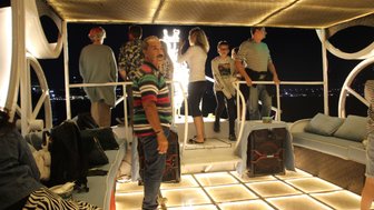 Familien sitzen auf einer beleuchteten Feluke während einer nächtlichen Fahrt auf dem Nil – Ägypten Reise mit Kindern