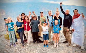 Reisegruppe posiert gemeinsam mit ihrem Guide vor der Bergkulisse des Jebel Shams – Oman Reise mit Kindern