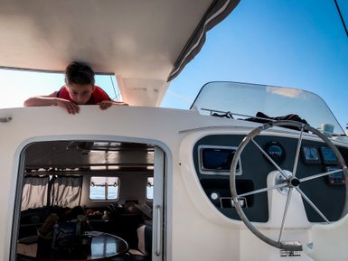 Ein Junge mit einer Rettungsweste lehnt über die Reling eines Segelboots und schaut neugierig nach draußen.