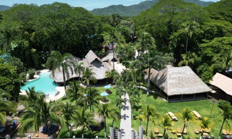 Ein tropisches Resort mit einem glitzernden Pool, umgeben von üppigem Grün und Palmen, lädt zum Entspannen ein.