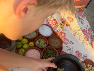 Ein Kind zerdrückt Trauben in einem Mörser, um frische Aromen für ein Gericht zu erzeugen, umgeben von verschiedenen Gewürzen.