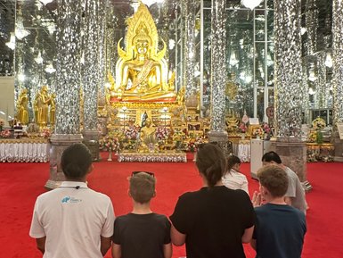 Familie schuat kniend auf den goldenen Buddha im Kristalltempel in Uthai Thani - Thailand mit Kindern