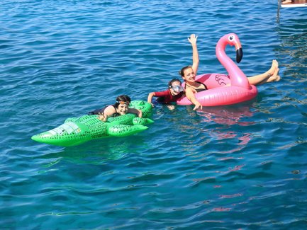 Drei Kinder genießen das Schwimmen im klaren Wasser, während sie auf bunten Luftmatratzen entspannen und lachen.