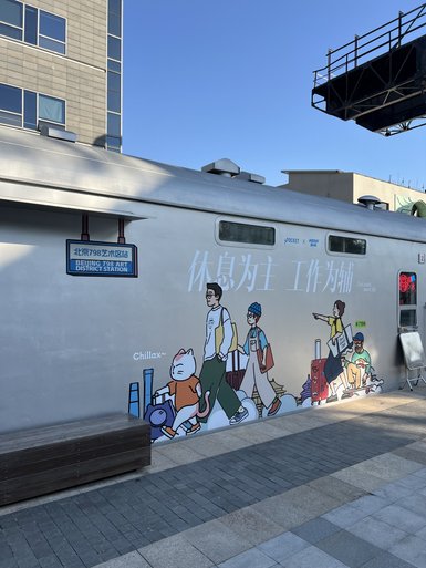 Eine bunte Wandmalerei zeigt eine Gruppe von Menschen und einem Kätzchen, die mit Gepäck in einem kreativen Stadtteil unterwegs sind.