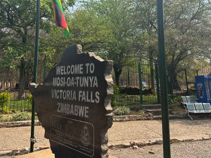 Ein markanter Stein mit der Aufschrift 'Willkommen in Mosi-oa-Tunya, Victoriafälle, Simbabwe' steht im Freien.