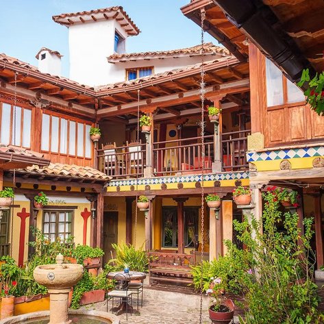 Ein malerischer Innenhof mit bunten Blumen und einem Brunnen, umgeben von traditioneller Architektur und Holzverzierungen.