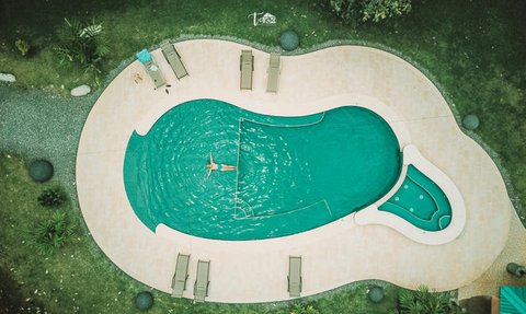 Ein Schwimmer entspannt in einem ausladenden Pool, umgeben von Sonnenliegen und üppiger Pflanzenwelt.