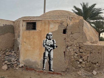 Ein Stormtrooper aus Pixelkunst steht an einer verwitterten Wand eines alten Gebäudes in einer trockenen Umgebung.