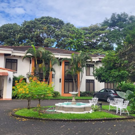 Ein elegantes Hotelgebäude mit einem einladenden Eingangsbereich und üppiger Vegetation umgibt die gepflegte Landschaft.