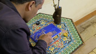Ein Künstler konzentriert sich auf die Miniaturmalerei, während er feine Details auf einer blauen Fläche hinzufügt.