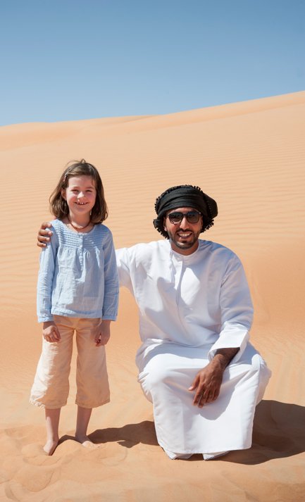 Mädchen steht neben einem Beduinen in der Wüste Omans – Oman mit Kindern