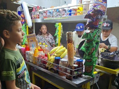Ein Junge steht an einem bunten Straßenstand, der mit Snacks, Getränken und frischen Früchten gefüllt ist.