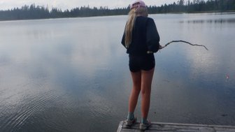 Eine Person steht am Ende eines Holzstegs und blickt nachdenklich auf einen ruhigen See unter einem bewölkten Himmel.