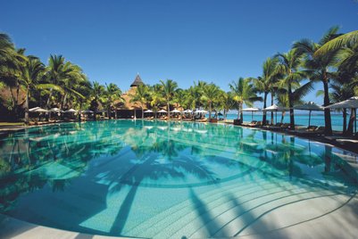 Ein glitzernder Pool spiegelt die Palmen und den strahlend blauen Himmel wider, umgeben von einem tropischen Paradies.