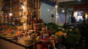 Ein lebhafter Marktstand mit einer Vielzahl von frischem Gemüse, eingelegten Lebensmitteln und bunten Gewürzen in Gläsern.
