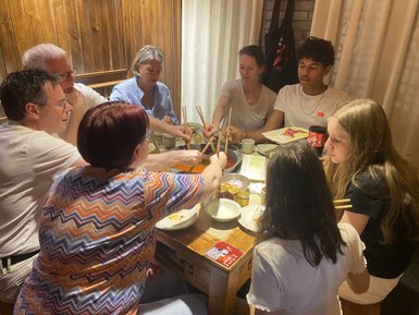 Eine Gruppe von acht Personen sitzt um einen Tisch und genießt gemeinsam ein Essen mit Stäbchen in einem gemütlichen Raum.
