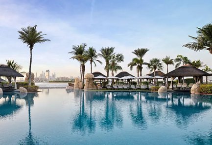 Ein ruhiger Poolbereich mit Palmen und Liegen, der die Skyline von Dubai im Hintergrund spiegelt.