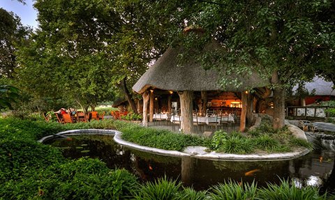 Ein einladendes Restaurant mit Strohdach, umgeben von üppigem Grün und einem ruhigen Teich, der die Natur widerspiegelt.