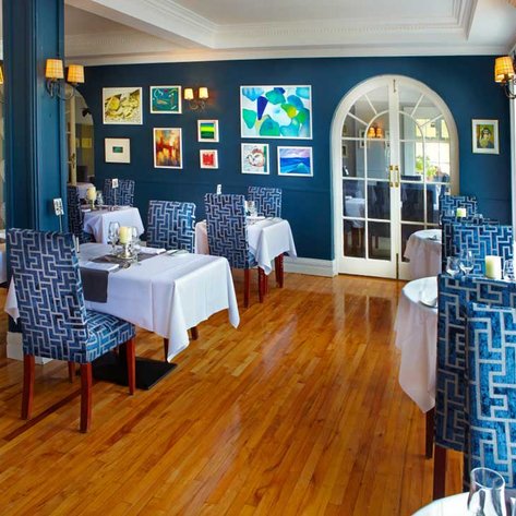 Ein elegantes Restaurant mit blauen Wänden, stilvollen Stühlen und kunstvollen Bildern an den Wänden, das eine einladende Atmosphäre schafft.