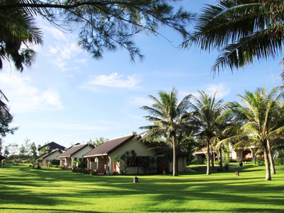 Eine ruhige Gartenlandschaft mit Palmen und mehreren Bungalows, die in der Sonne stehen und eine entspannte Atmosphäre schaffen.