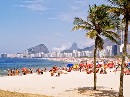 Ein sonniger Strand von Copacabana mit vielen Menschen, farbigen Sonnenschirmen und einer tollen Kulisse von Gebäuden.