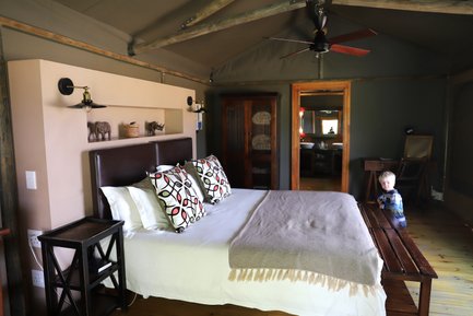 Ein gemütliches Schlafzimmer mit einem großen Bett, bunten Kissen und einem kleinen Jungen, der neugierig im Raum steht.