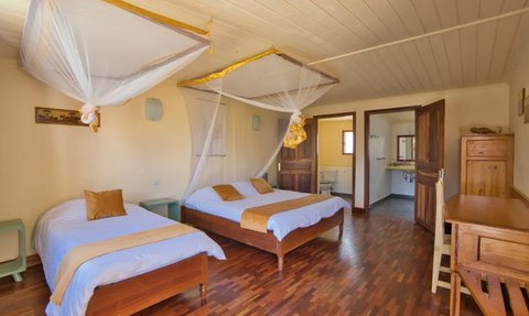 Ein helles Zimmer mit zwei Betten, umgeben von Moskitonetzen, und einem Holzfußboden, der eine warme Atmosphäre schafft.