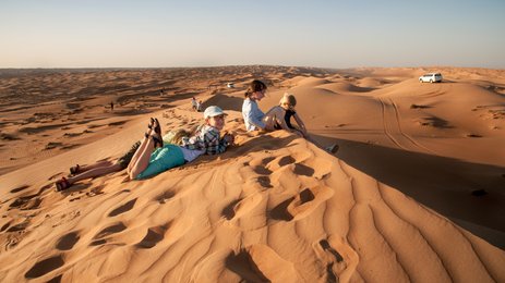 Kinder sitzen gemeinsam auf einer Wüstendüne – Oman Familienreise