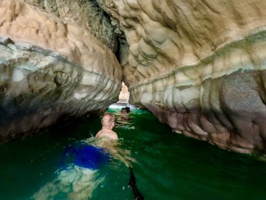 Familie schwimmt im Wasser zwischen Felsen im Wadi Shab – Oman Reise mit Kindern