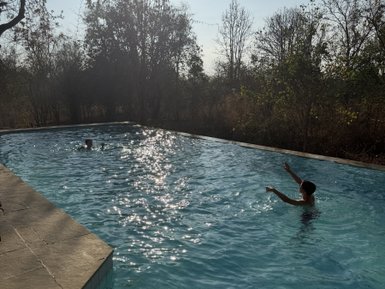 Ein Junge plantscht fröhlich im glitzernden Wasser eines Pools, umgeben von strahlendem Sonnenlicht und Bäumen.