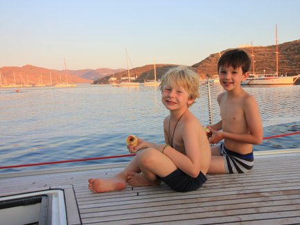 Zwei fröhliche Jungen sitzen auf dem Deck eines Bootes und genießen frisches Obst, während die Sonne untergeht.