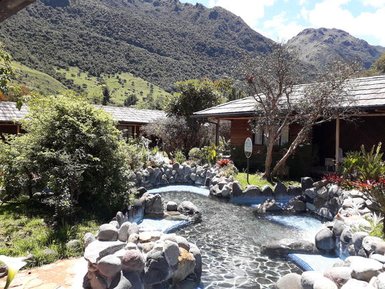 Eine malerische Landschaft mit einem klaren Wasserlauf, umgeben von üppigem Grün und rustikalen Holzhütten.