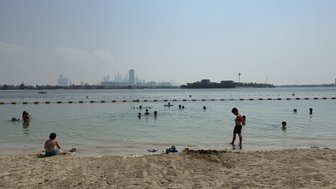 Ein Junge steht am Strand und spielt im flachen Wasser, während andere Kinder im Hintergrund schwimmen und sich amüsieren.