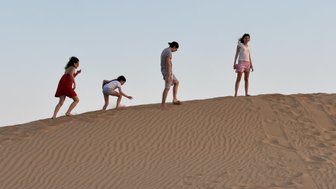 Vier Personen erkunden eine Sanddüne, während die Sonne am Horizont untergeht, was eine entspannte Atmosphäre schafft.