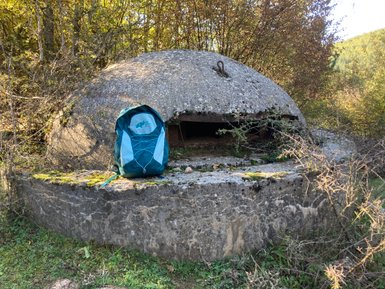 Ein verlassener Bunker mit einer runden, moosbedeckten Betonoberfläche, umgeben von üppigem Grün und Bäumen.