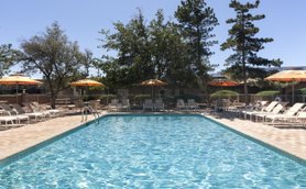 Ein einladender Pool mit klarem Wasser, umgeben von Liegen und Sonnenschirmen, unter einem strahlend blauen Himmel.