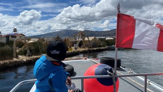 Ein Junge sitzt auf einem Boot und blickt auf die schwimmenden Inseln des Titicaca-Sees, umgeben von Bergen und Wolken.