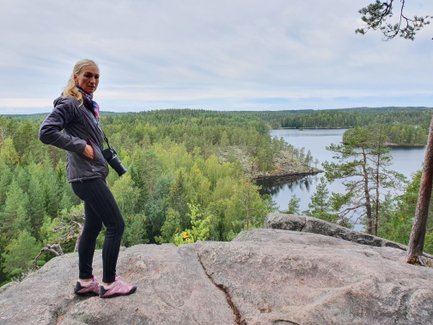Eine Frau steht auf einem Felsen und blickt auf einen malerischen See, umgeben von dichten, grünen Wäldern.
