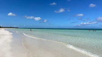 Ein ruhiger Strand mit feinem, weißen Sand und klarem, türkisfarbenem Wasser unter einem strahlend blauen Himmel.