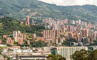 Eine beeindruckende Aussicht auf Medellín, mit hohen Wohngebäuden, die sich an den Berghang schmiegen und üppigem Grün im Vordergrund.