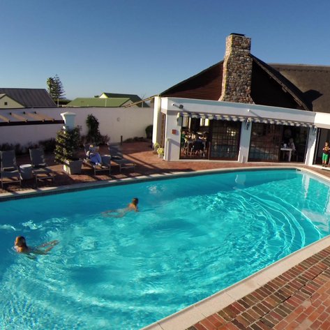 Zwei Kinder schwimmen fröhlich in einem solarbeheizten Pool, umgeben von einer einladenden Lodge und sonnigem Himmel.