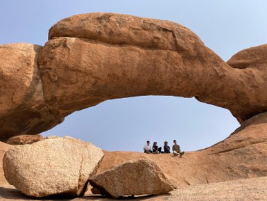 Eine Reisegruppe sitzt gemeinsam unter einem imposanten Felsbogen - Namibia mit Kindern