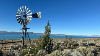 Eine alte Windmühle steht majestätisch vor dem klaren blauen Wasser des Lago Argentino, umgeben von sanften Hügeln.