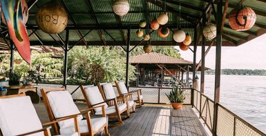 Eine einladende Veranda mit weißen Stühlen, umgeben von üppigem Grün und bunten Lampen, die eine entspannte Atmosphäre schaffen.