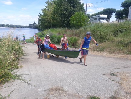 Eine Gruppe von Menschen zieht ein Kanu mit Gepäck am Ufer eines Flusses entlang, umgeben von üppigem Grün.