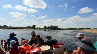 Eine Gruppe von Menschen sitzt in einem Kanu und genießt einen sonnigen Tag auf einem ruhigen Fluss mit blauen Himmel.