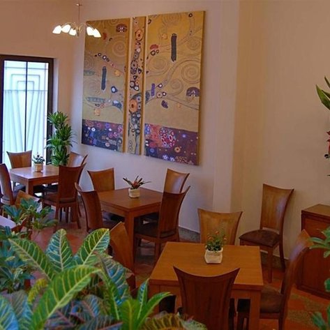 Ein stilvolles Restaurant mit Holztischen und Stühlen, umgeben von Pflanzen und einer bunten Wandmalerei.