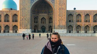 Eine Frau steht lächelnd vor der beeindruckenden Architektur des Registan in Samarkand, umgeben von Besuchern.