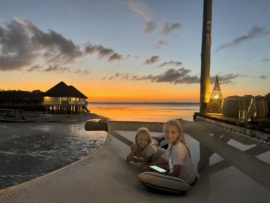 Zwei Mädchen sitzen auf einer Hängematte und genießen den Sonnenuntergang über dem Wasser, umgeben von einer ruhigen Atmosphäre.