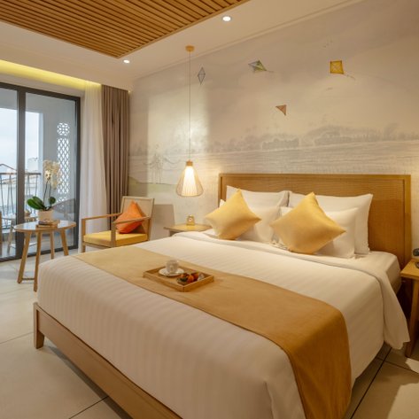 Ein stilvolles Hotelzimmer mit einem großen Bett, dekoriert mit gelben Kissen und einem kleinen Tisch mit Obst und einer Tasse.